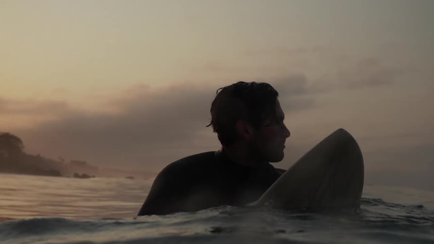 A man rides a surfboard near sunset