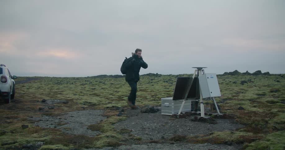 Man wearing coat walks from suv to equipment in moss covered field