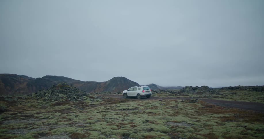 A white automobile is traveling on a rural road with mountains in the distance