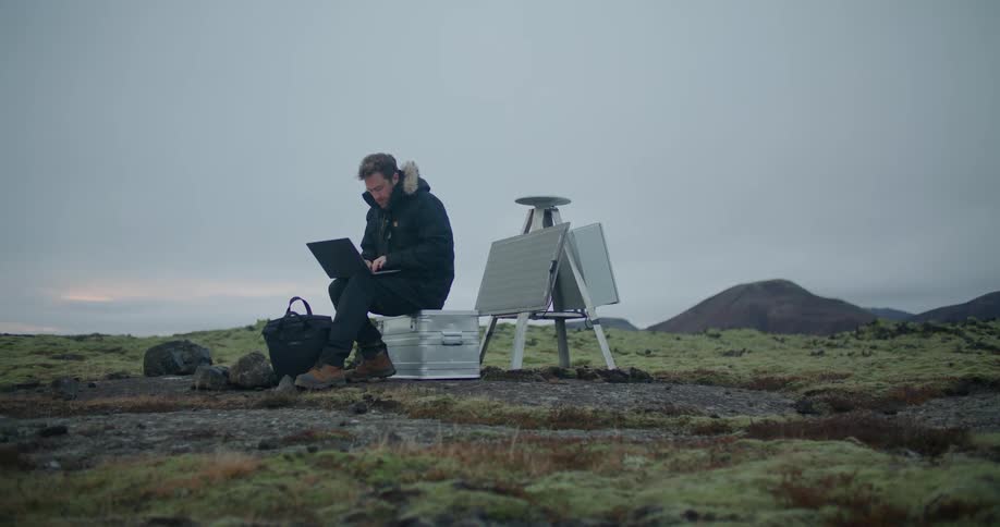 A man sits in a field and types on a laptop