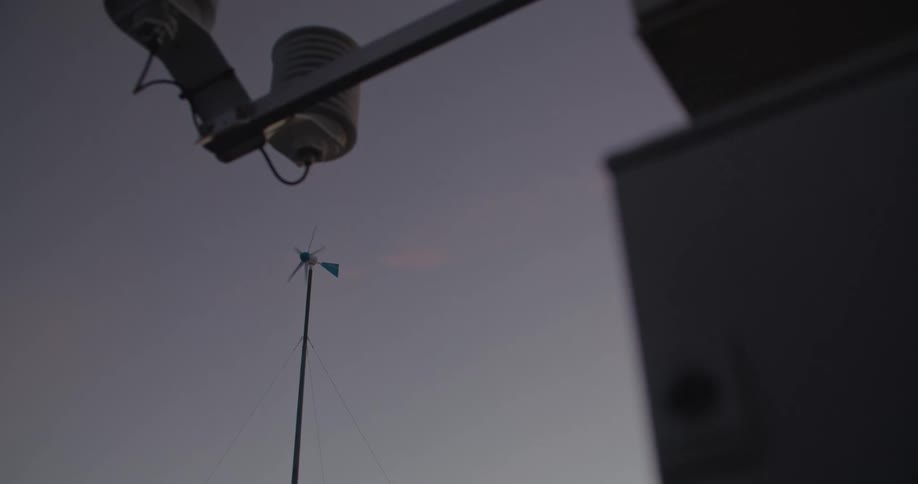 Outdoor electric power pole stands near pole with rotating propeller under clear sky