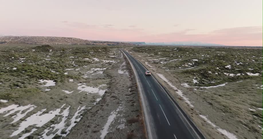 A car travels along a road through a vast countryside at sunset