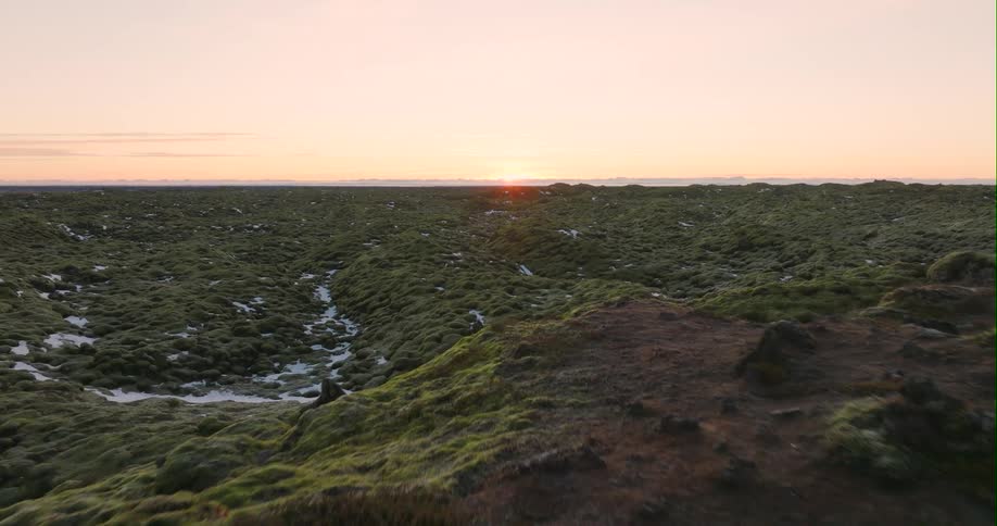 Snow speckled moss covered terrain stretches to the horizon under a red sky