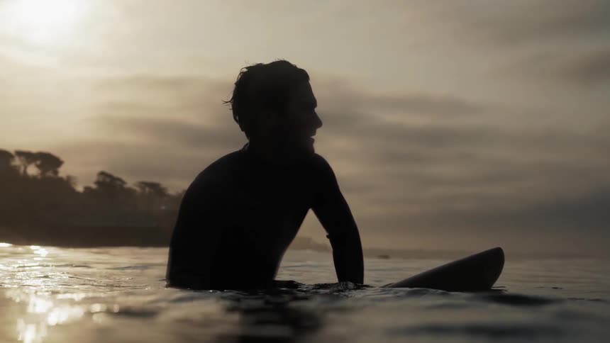A man sits on a surfboard at sunset