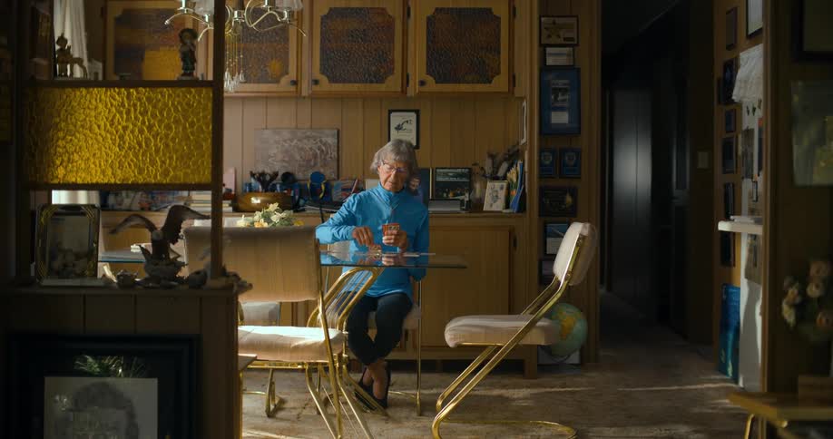 Grandmother playing a game of solitaire on the glass table in the living room at home