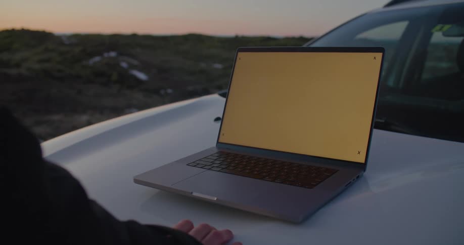 Someone is looking at a laptop computer sitting on the hood of an automobile