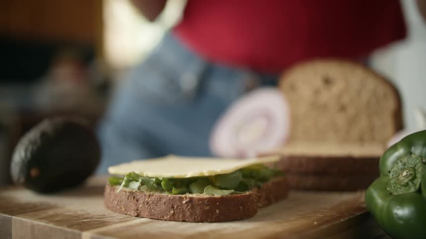 Woman with red shirt and jeans makes sandwich on cutting board in the kitchen