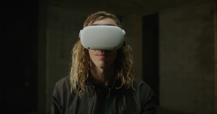A man with long blond hair has a virtual reality headset on his head and he pulls it down over his eyes