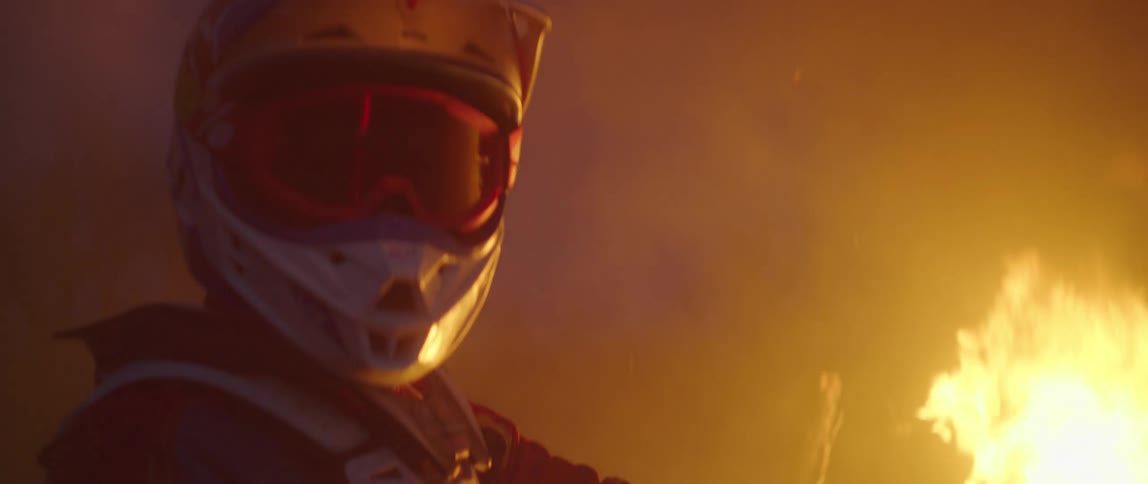 Person wearing helmet and goggles sits on bike near roaring smoking bonfire
