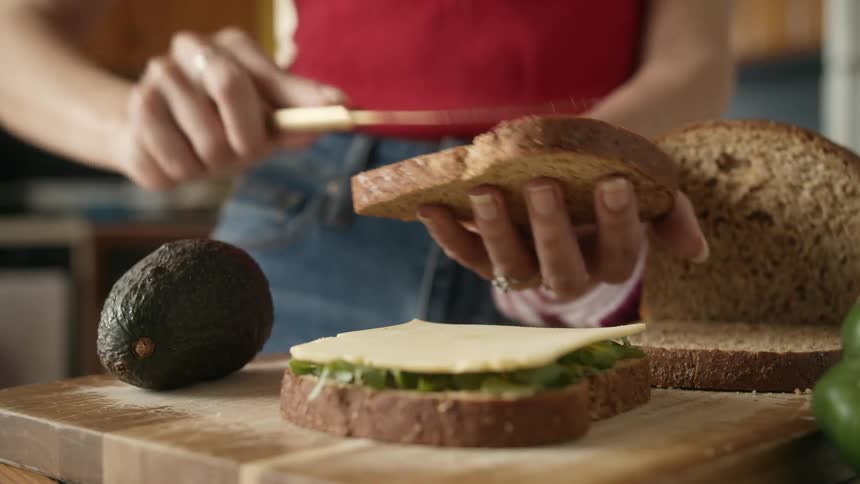 Woman with red shirt and jeans makes sandwich in the kitchen
