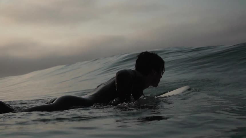 A man paddles on his surfboard into a wave
