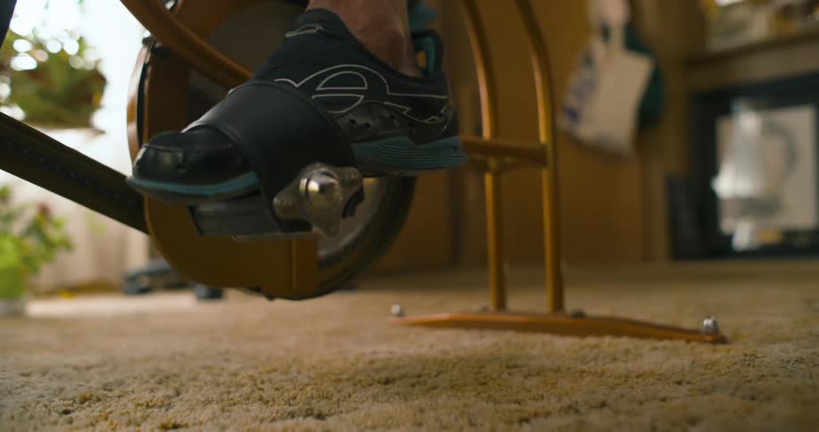 A person in athletic shoes puts their foot into a pedal strap on a stationary bike