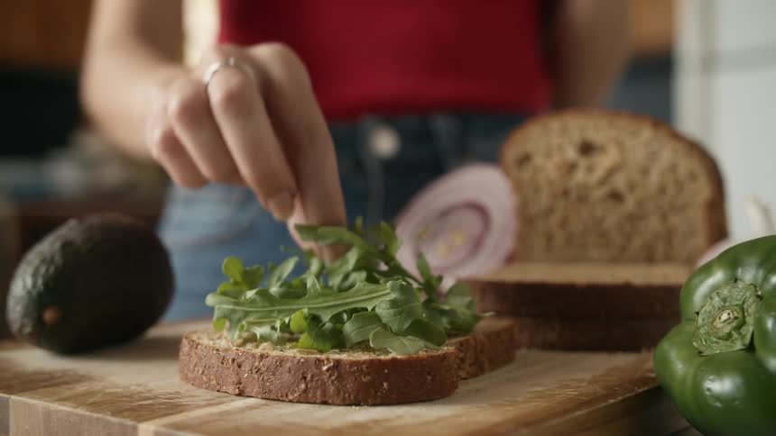 Woman with red shirt and jeans makes sandwich in the kitchen