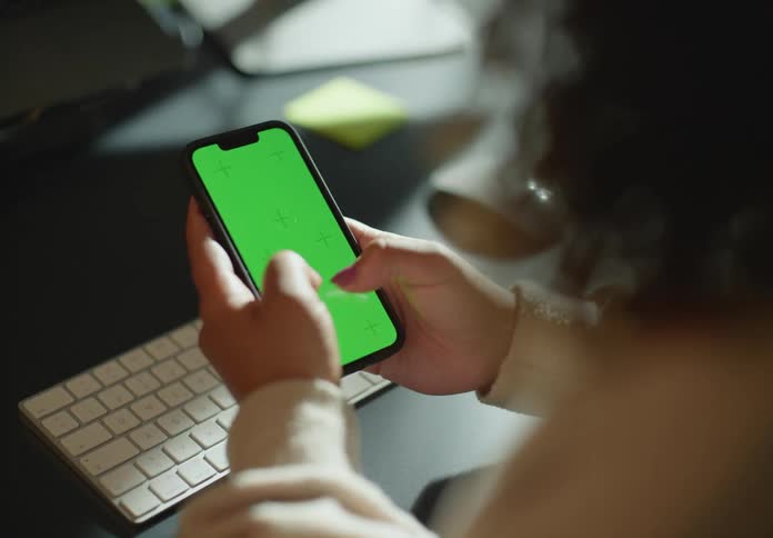 Young woman sitting at a desk typing on a smartphone with a green replaceable screen
