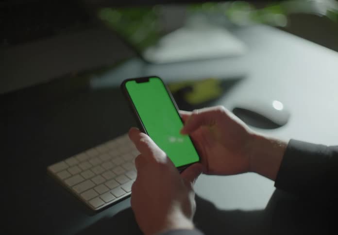 Person typing on computer keyboard stops to pick up and scroll on their mobile phone