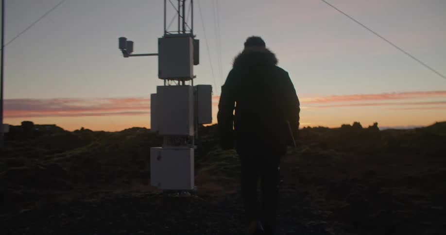 A man wearing a winter coat walks to a utility pole and looks at the utility boxes