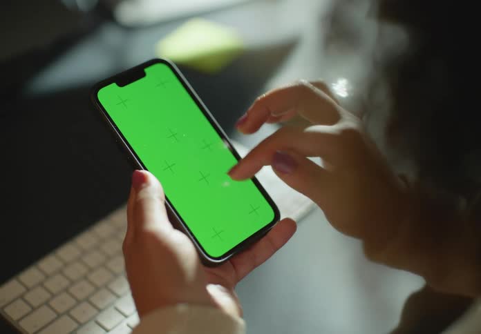 Woman sitting at a desk in the office using a smartphone with green replaceable screen