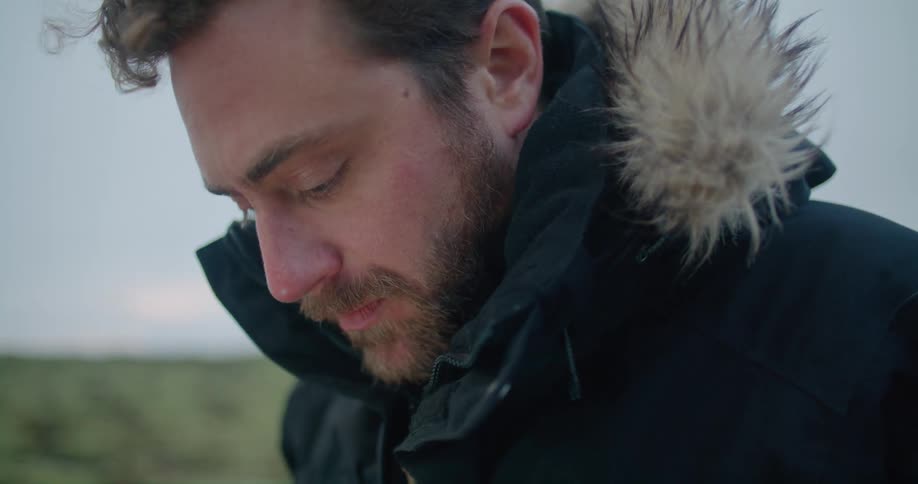 A man wears a parka with a thick fur collar as he stands in a field