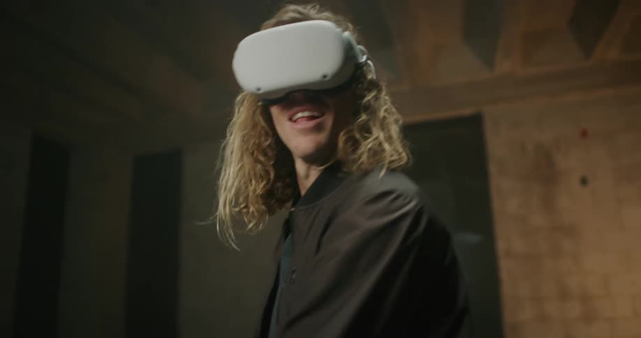 Man wearing vr headset in room with exposed rafters plays game using two game controllers