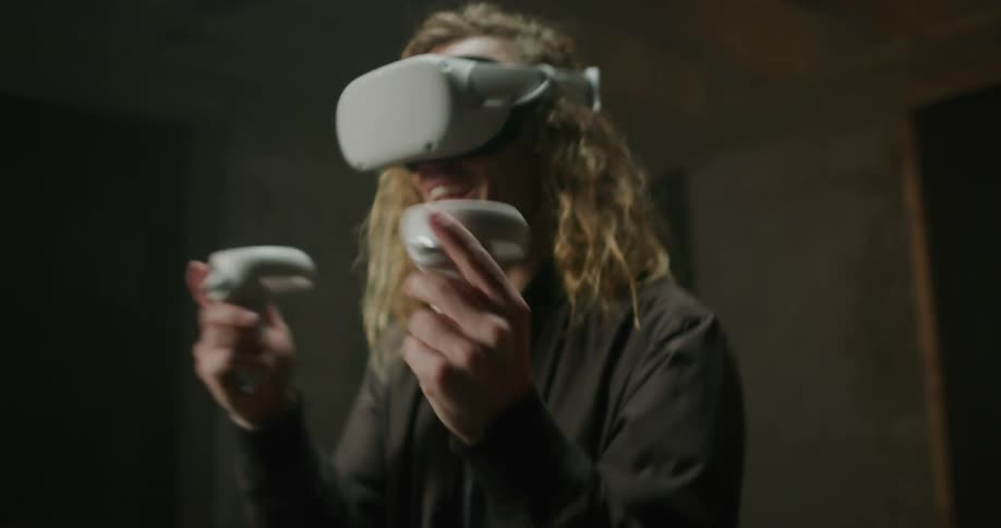 Blonde man holding controllers swinging his arms playing a virtual reality game
