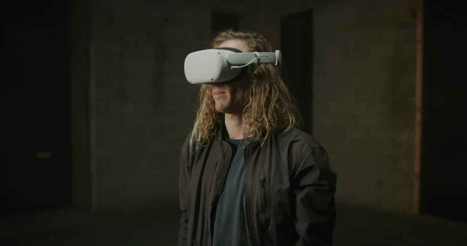 A man with long blond hair has a virtual reality headset on his head and he pulls it down over his eyes