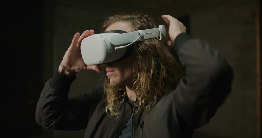 Young blonde long haired man puts on 3d virtual reality goggles over his eyes