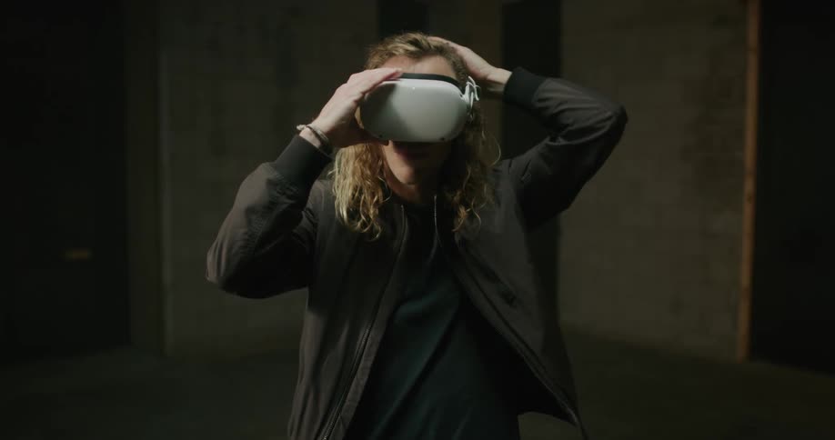 A man with long blond hair puts on a virtual reality headset