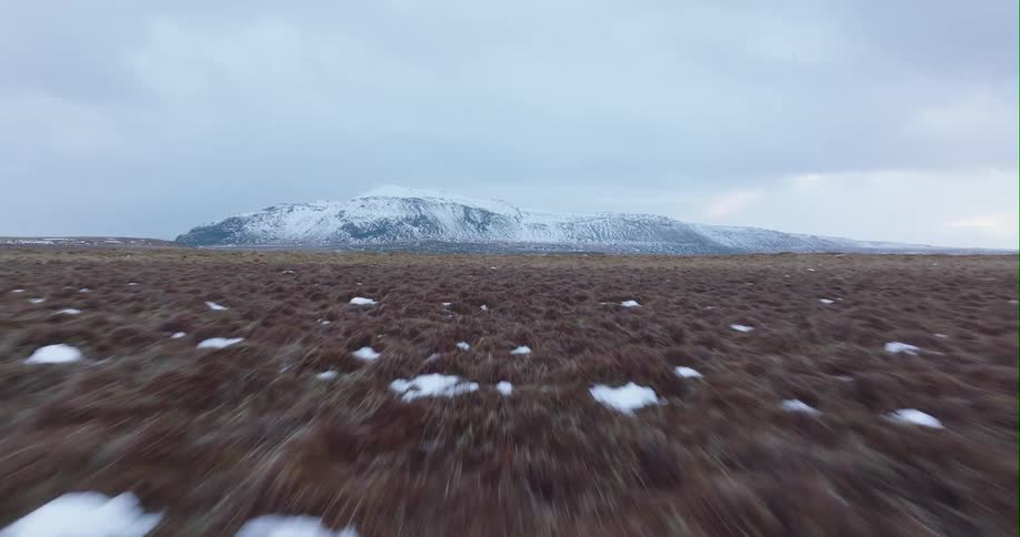 Light snow is on the ground and a snow covered mountain range is on the other side of a lake