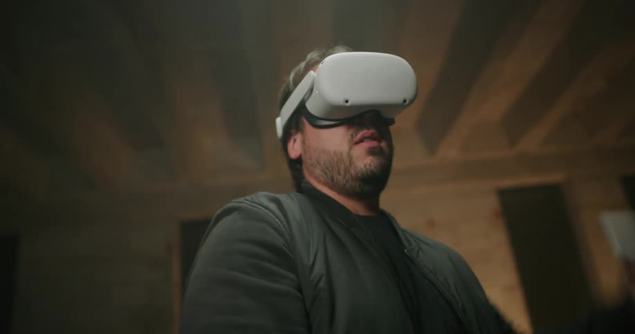 A man wearing virtual reality goggles is holding controllers and swinging his arms as he plays a game