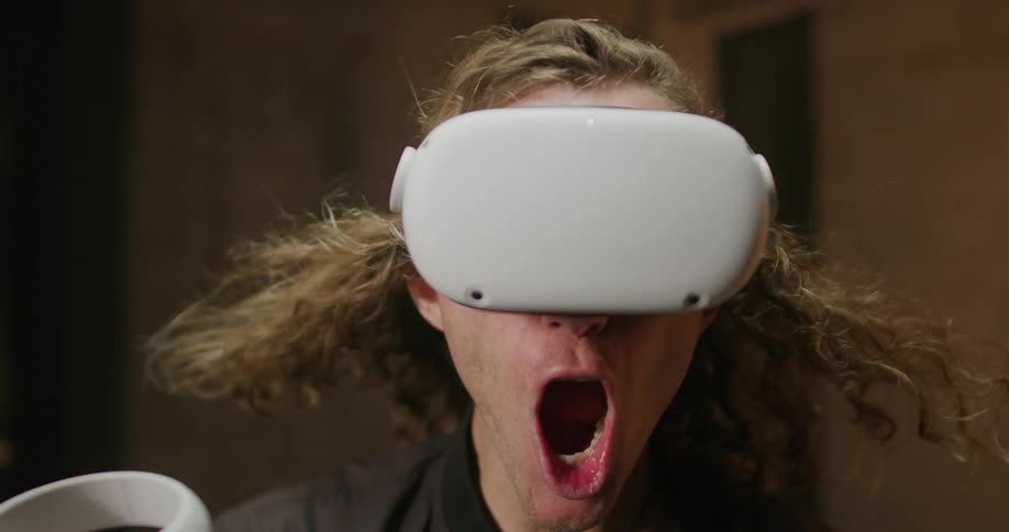 A man shouts while using a virtual reality headset as wind whips through his hair and lights flash above him