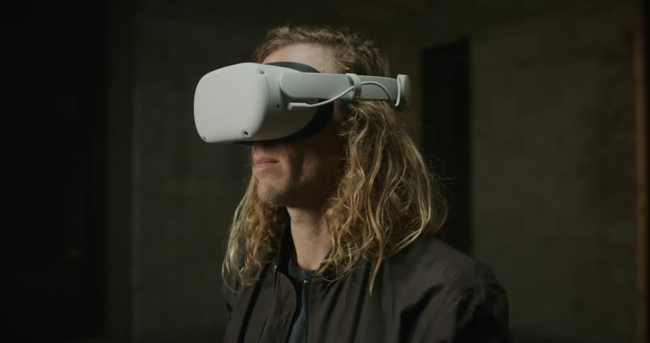 Young blonde long haired man puts on 3d virtual reality goggles over his eyes