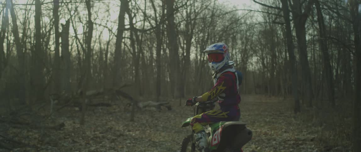 A man is dirt biking in the woods at dusk