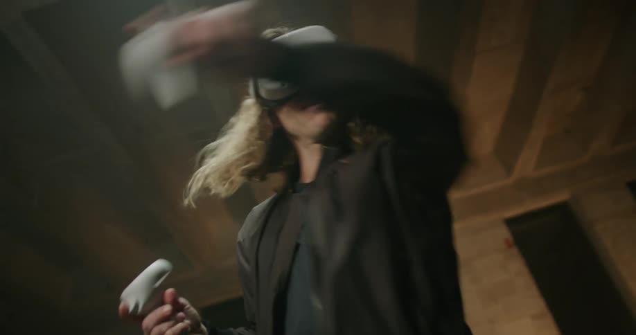 Blonde curly haired man playing a virtual reality game in a vacant room
