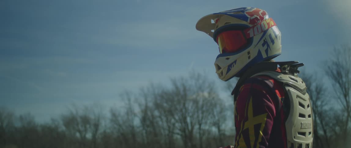 A person wearing a helmet and goggles and dirt biking gear is outside on a sunny day