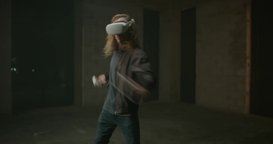 A teenager with a virtual reality headset on swings his arms around as he plays