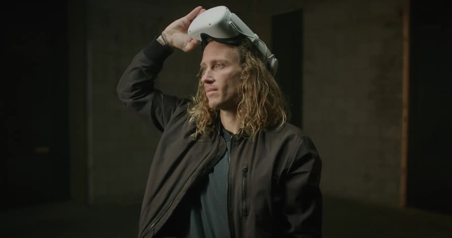 Blonde man standing in empty room raises vr headset