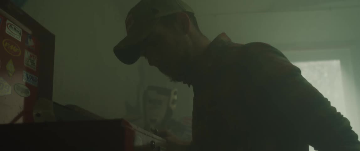 Man searches through tool chests drawers in dimly lit workshop