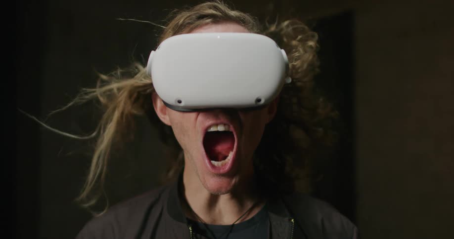 Man wearing 3d virtual reality goggles screams while his hair is blowed by the wind
