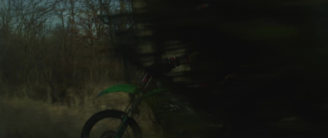 A person rides an offroad motorcycle through a woodland during the day