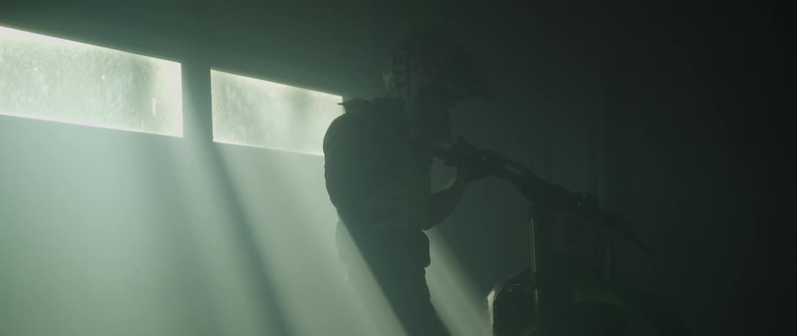 A man puts on a helmet then pushes a motorcycle through a room