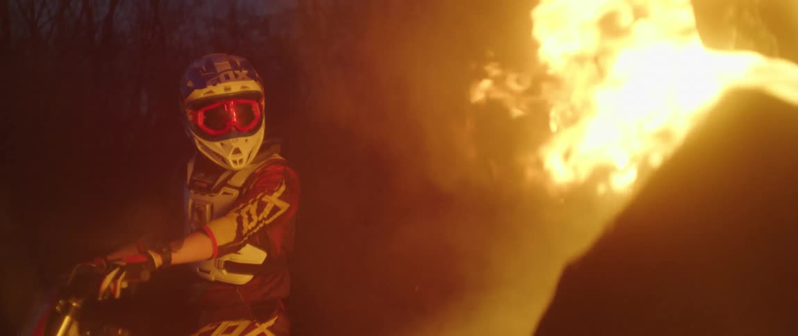 A motocross rider stands on his bike and watches a bonfire