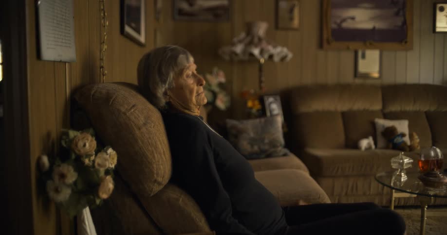 Elderly woman sits on sofa and looks down with her hands clasped