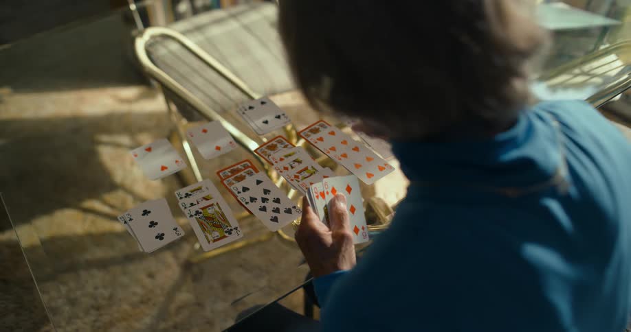 Elderly woman playing solitaire card game on the glass table at home