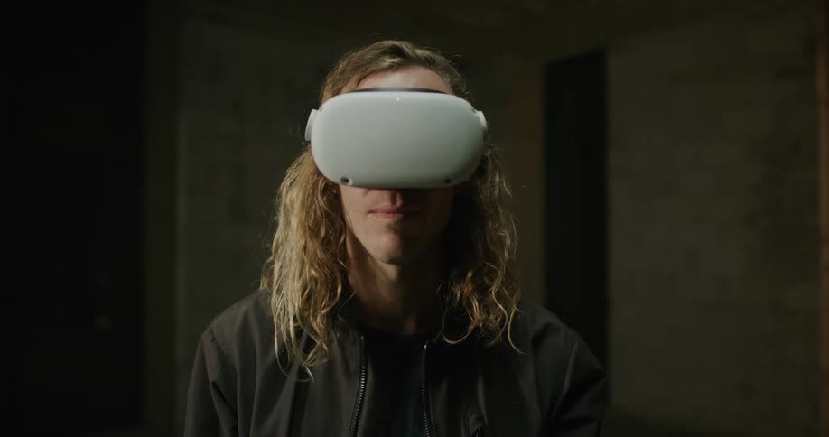 A man with long blond hair is wearing a virtual reality headset