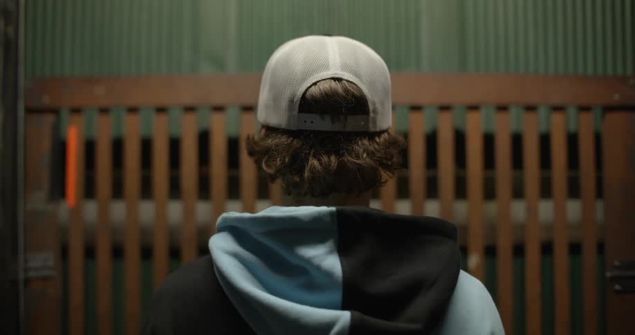 Man wearing hoodie and cap rides elevator with protective grill
