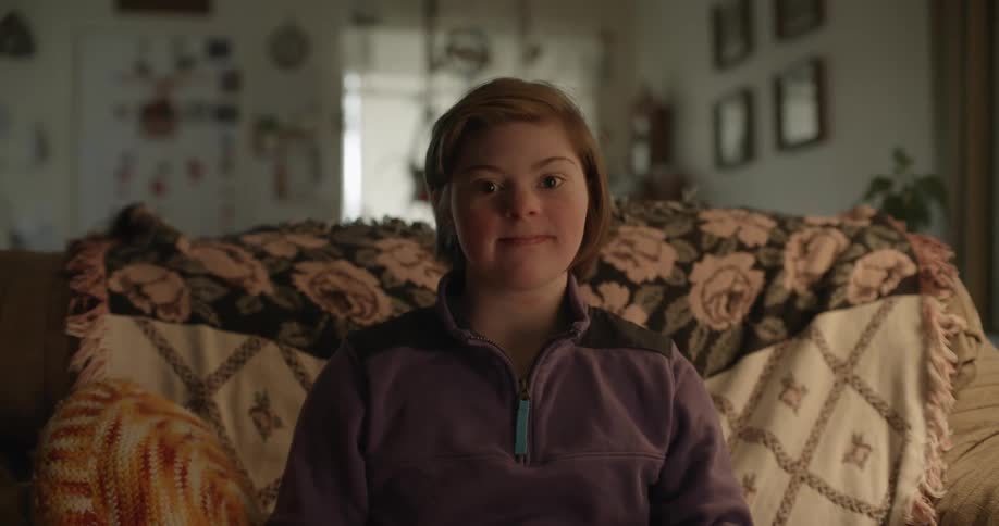 Girl with short hair and sweater sitting on couch looks at camera smiling in living room at home