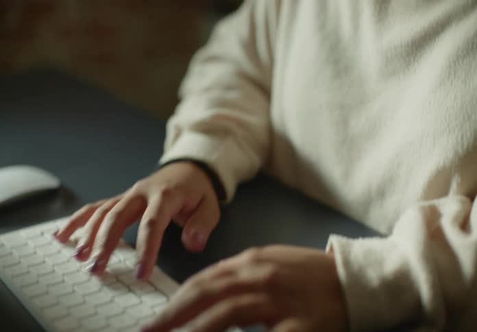 A woman is typing on a keyboard sitting on the desk in front of her