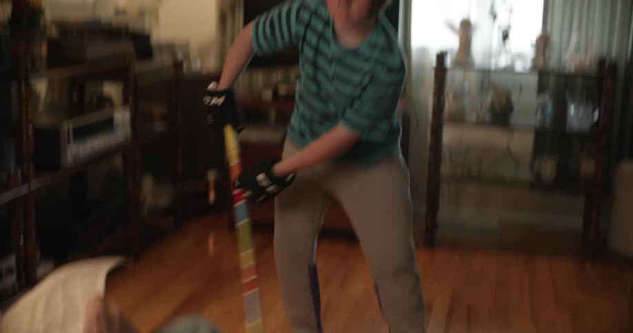 Young girl practices hockey with a broom in front of her father reading a newspaper