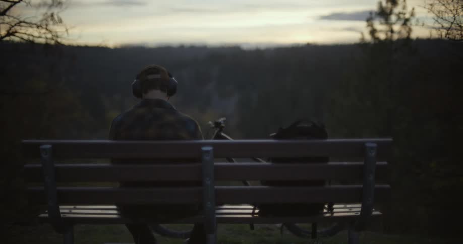 A man listens to headphones while sitting on a bench in a forest