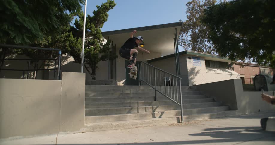 A skateboarder with a prosthetic leg jumps down a staircase on his skateboard as another man films him with a smartphone